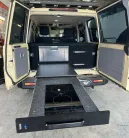 Evakool 40L Platinum Drawer10 > 4wd Lights and Camping Online Store Campervan rear with a pull-out kitchen: black countertop, two-burner induction stove, and fridge drawer inside open doors